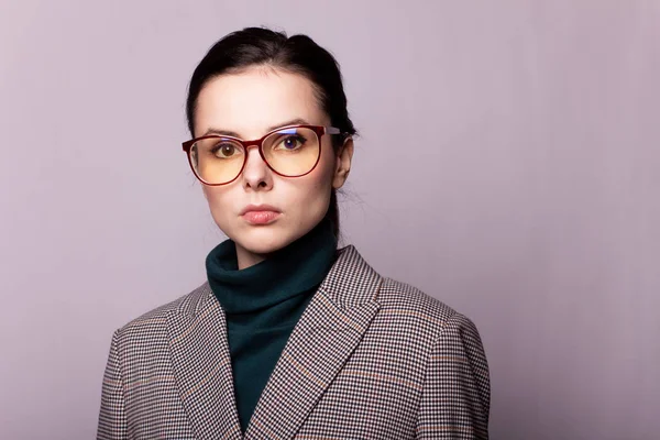 girl in a green turtleneck, jacket, glasses, portrait on a gray background