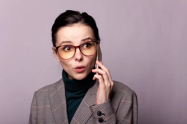 girl in a green turtleneck, jacket, glasses talking on the phone portrait on a gray background