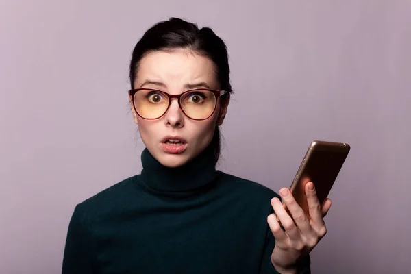 girl in a green turtleneck and glasses for sight communicates on the phone, portrait on a gray background