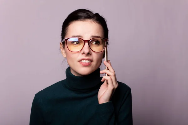 girl in a green turtleneck and glasses for sight communicates on the phone, portrait on a gray background