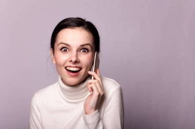 Beyaz balıkçı yakalı bir kız telefonla konuşuyor, gri arka planda bir portre.