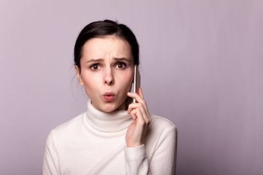 Beyaz balıkçı yakalı bir kız telefonla konuşuyor, gri arka planda bir portre.