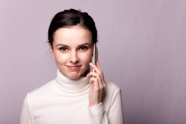 Beyaz balıkçı yakalı bir kız telefonla konuşuyor, gri arka planda bir portre.