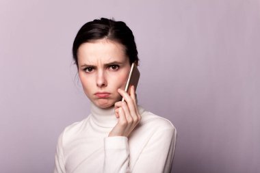 Beyaz balıkçı yakalı bir kız telefonla konuşuyor, gri arka planda bir portre.