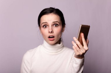 Beyaz balıkçı yakalı bir kız telefonla konuşuyor, gri arka planda bir portre.