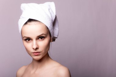 Kafasında beyaz havlu olan, gri arka planı olan bir kız.