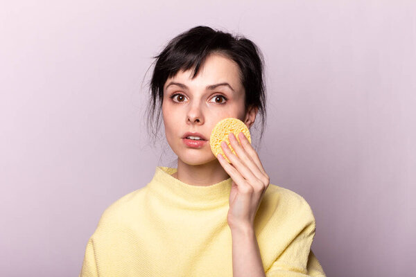 красивая девушка в желтом свитере держит губку в руках
