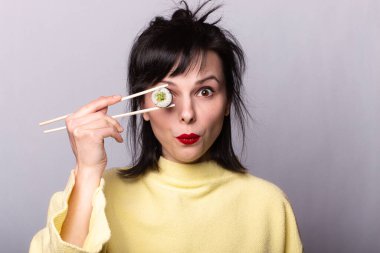 Sarı kazaklı komik kadın suşi yiyor. Çubuklardaki suşi