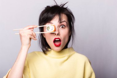 Dudaklarında sarı bir süveter olan kırmızı rujlu kız Japon usulü suşi tutuyor.