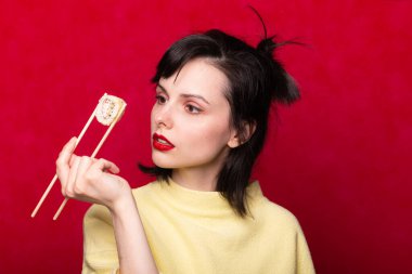 Dudaklarında sarı bir süveter olan kırmızı rujlu kız Japon usulü suşi tutuyor.