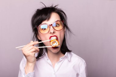 Dudaklarında kırmızı ruj olan kız öğrenci ellerinde çubuklarla Japon usulü suşi tutuyor.