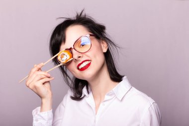 Dudaklarında kırmızı ruj olan kız öğrenci ellerinde çubuklarla Japon usulü suşi tutuyor.