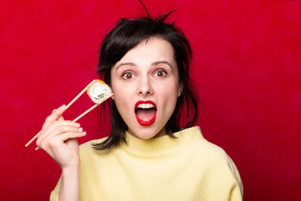 Woman eating sushi and rolls on a red background
