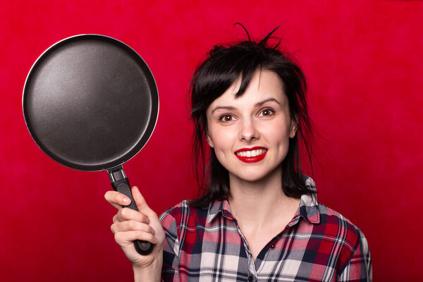 Женщина с красными губами держит сковородку в руках, красный фон
