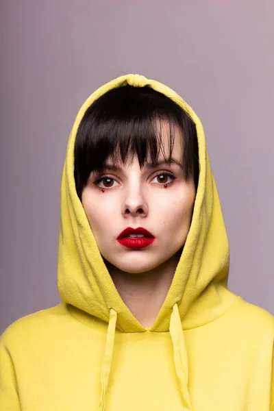 woman in a hoodie with red lipstick on the lips and dots under the eyes