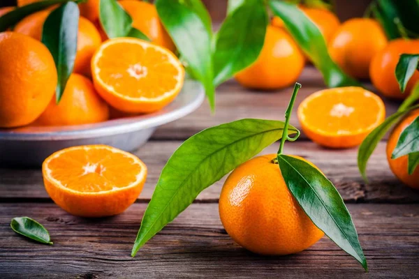 Saftigt mogna mandariner med blad i en skål på trä bakgrund. — Stockfoto