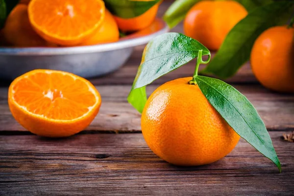 Saftigt mogna mandariner med blad i en skål på trä bakgrund. — Stockfoto