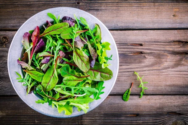 Fresh salad with mixed greens on wooden background — Stock Photo, Image