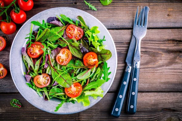 Salada fresca com verduras mistas e tomate cereja em fundo de madeira — Fotografia de Stock