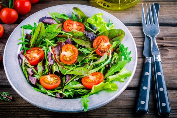 Свежий салат со смешанной зеленью и помидорами черри на деревянном фоне — стоковое фото