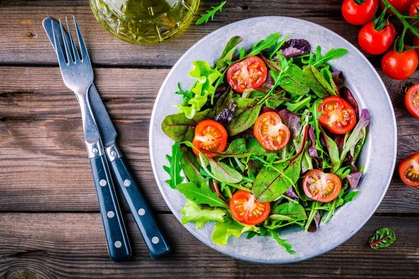 Свежий салат со смешанной зеленью и помидорами черри на деревянном фоне — стоковое фото