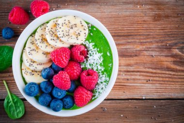 Sağlıklı kahvaltı kase: muz, böğürtlen, ahududu, chia tohum ve Hindistan cevizi ile yeşil ıspanak güler yüzlü