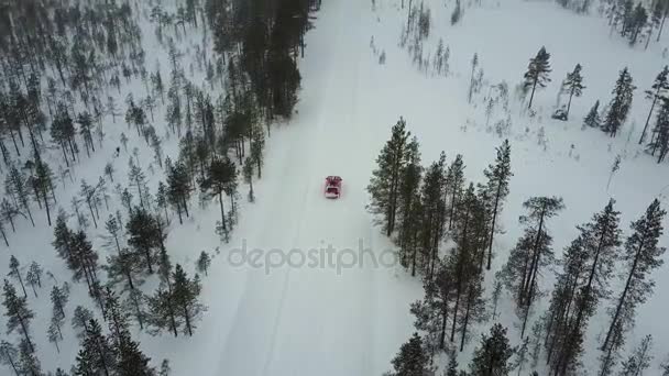 降雪時のラップランドの美しい冬の風景の道で唯一の赤車の眺め.車の線形追跡。空撮. — ストック動画