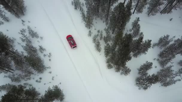 Vista aérea del único coche rojo en la carretera en el hermoso paisaje invernal de Laponia durante una nevada. Rastreando un auto retirado. Vídeo aéreo . — Vídeos de Stock