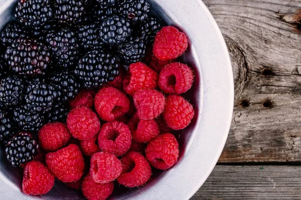 Fresh ripe organic raspberries and blackberries closeup in a bowl on a wooden background — Stock Photo, Image