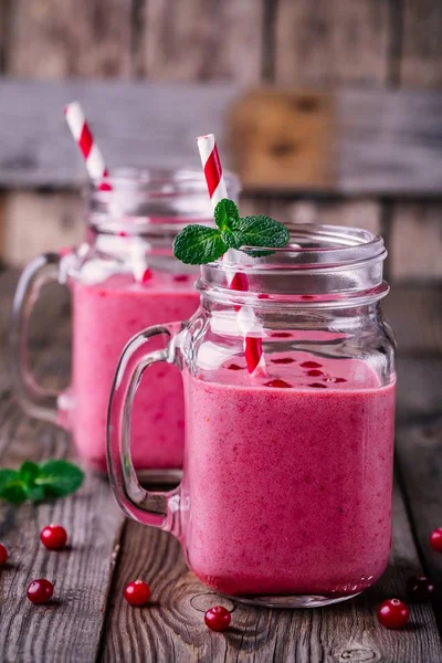 Pink smoothie with wild cranberries in mason jar with mint and straw on wooden background — Stock Photo, Image