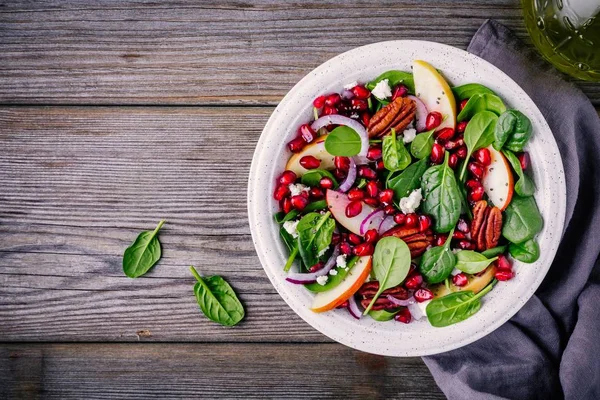 Salade maison d'épinards, pommes, pacanes, oignons rouges au fromage de chèvre et grenade sur fond de bois — Photo