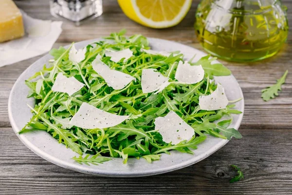 Ensalada de rúcula verde con queso parmesano, limón, aceite de oliva y condimentos —  Fotos de Stock