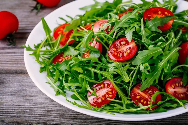 Salada verde fresca com arugula e tomates vermelhos no fundo de madeira — Fotografia de Stock