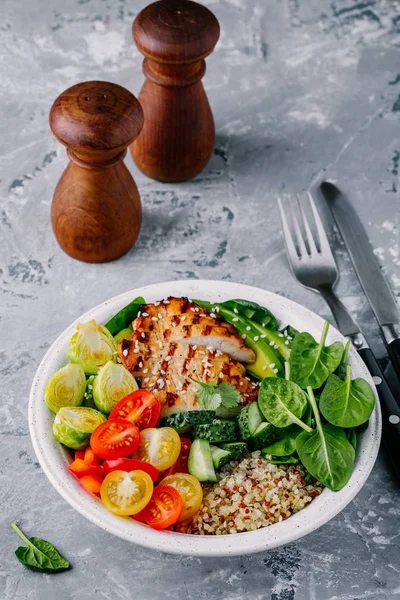 Gezonde lunch van de kom van de Boeddha met gegrilde kip, quinoa, spinazie, avocado, spruiten, tomaten, komkommers op donkere grijze achtergrond. — Stockfoto