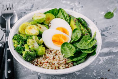 Sağlıklı yeşil vejetaryen Buda kase yumurta, quinoa, ıspanak, avokado, ile öğle yemeği ızgara Brüksel lahanası ve brokoli koyu gri arka plan üzerinde. 