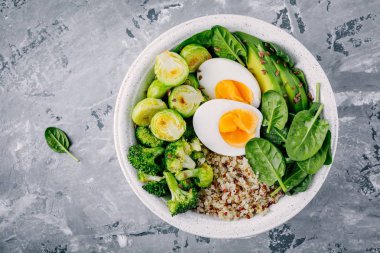 Sağlıklı yeşil vejetaryen Buda kase yumurta, quinoa, ıspanak, avokado, ile öğle yemeği ızgara Brüksel lahanası ve brokoli koyu gri arka plan üzerinde. 