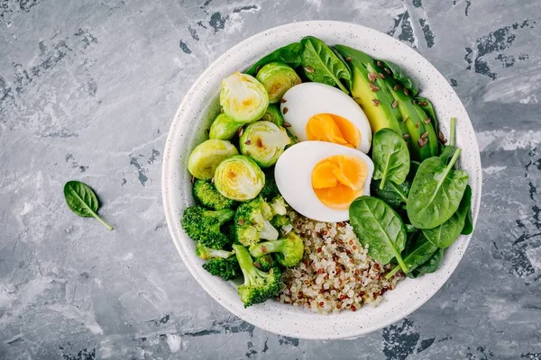 Sağlıklı yeşil vejetaryen Buda kase yumurta, quinoa, ıspanak, avokado, ile öğle yemeği ızgara Brüksel lahanası ve brokoli koyu gri arka plan üzerinde. 