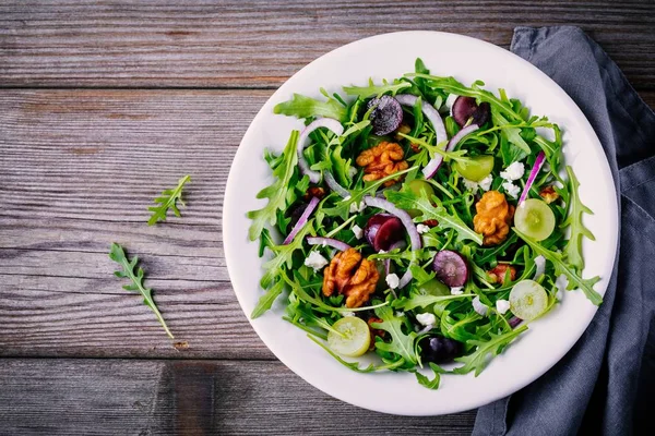 Green salad bowl with arugula, walnuts, goat cheese, red onion and grapes — Stock Photo, Image