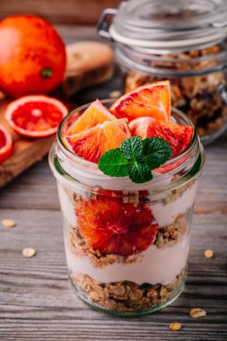 sağlıklı kahvaltı Cam Kavanoz yoğurt parfait ev yapımı granola ve kanlı bir ahşap arka plan üzerinde turuncu