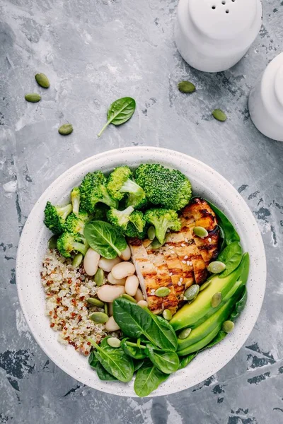 Green buddha bowl lunch with grilled chicken and quinoa, spinach, avocado, broccoli and white beans