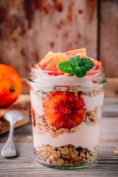 健康早餐玻璃罐酸奶糕与自制燕麦和血橙在木质背景 — 图库照片