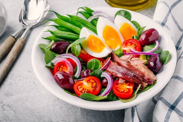 Салат с тунцом, анчоусами, яйцами, зеленой фасолью, оливками, помидорами, красным луком и листьями салата — стоковое фото