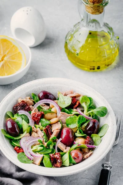 Salat mit weißen Bohnen, Thunfisch, Oliven, roten Zwiebeln und getrockneten Tomaten mit grünen Salatblättern — Stockfoto