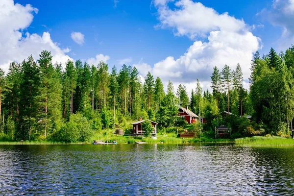Een traditionele Finse houten huisje met een sauna en een schuur op de oever van het meer. Landelijke Finland zomer. — Stockfoto
