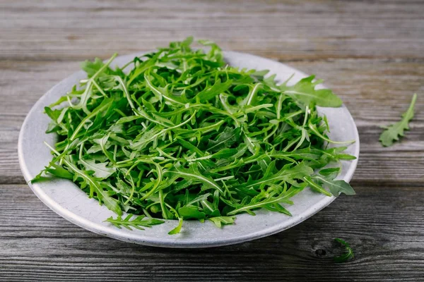 Fresh green arugula salad leaves in a bowl on a wooden background. — Stock Photo, Image