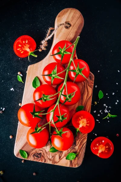 Um monte de tomates cereja orgânicos frescos com sal marinho e manjericão em placa de corte de azeitona — Fotografia de Stock