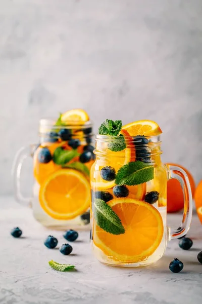 Água desintoxicada infundida com laranja, mirtilo e hortelã. Cocktail frio de verão ou limonada . — Fotografia de Stock