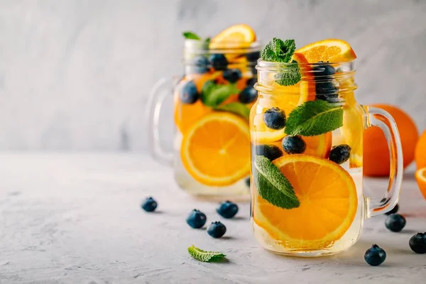 Água desintoxicada infundida com laranja, mirtilo e hortelã. Cocktail frio de verão ou limonada . — Fotografia de Stock