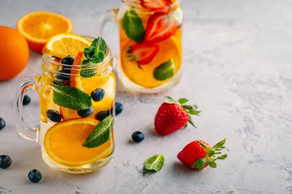 Água desintoxicada infundida com laranja, mirtilo, morango e hortelã. Cocktail frio de verão ou limonada . — Fotografia de Stock