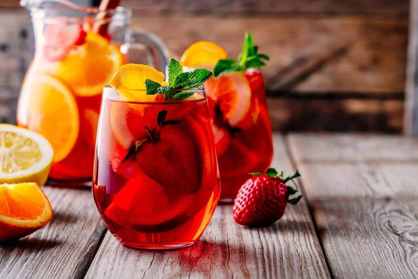 Homemade red wine sangria with orange, apple, strawberry and ice in glass and pitcher on wooden backgroun — Stock Photo, Image
